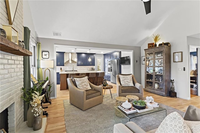 living room with visible vents, light wood-style flooring, a brick fireplace, and high vaulted ceiling