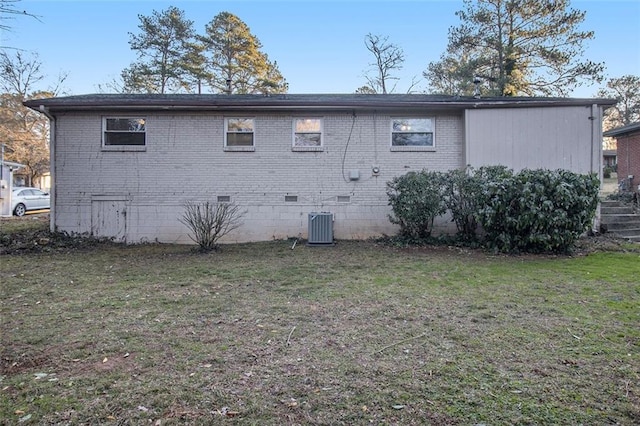 rear view of property with central air condition unit and a lawn