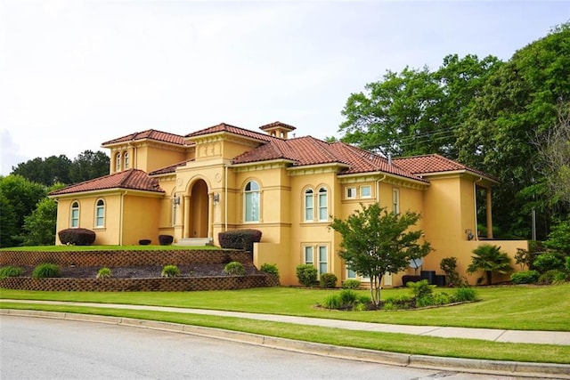 mediterranean / spanish-style home featuring a tiled roof, a front yard, and stucco siding