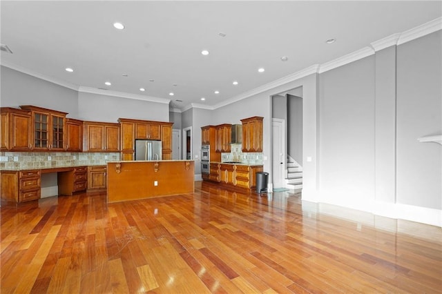 kitchen with a center island, brown cabinets, built in desk, light countertops, and appliances with stainless steel finishes