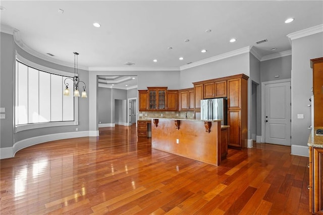 kitchen with visible vents, freestanding refrigerator, brown cabinets, a kitchen bar, and glass insert cabinets