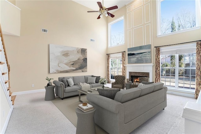 living area featuring light carpet, stairway, visible vents, and a high end fireplace