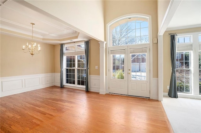 foyer entrance featuring a healthy amount of sunlight, light wood-style floors, ornamental molding, and french doors