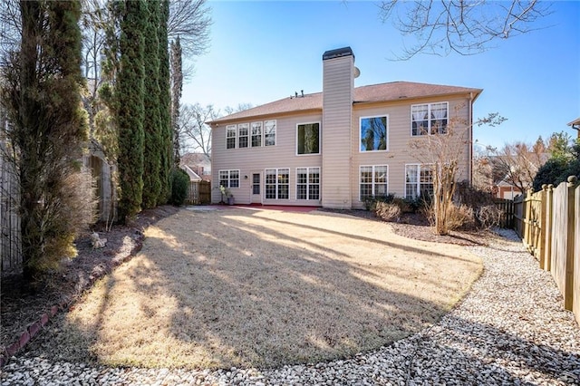 back of house with a fenced backyard, driveway, and a chimney