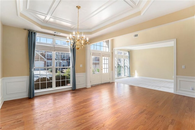 empty room featuring visible vents, coffered ceiling, light wood-style flooring, a decorative wall, and a notable chandelier