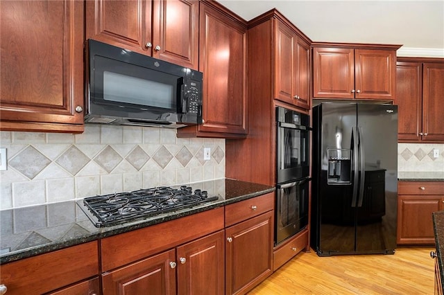 kitchen featuring black appliances, dark stone counters, light wood finished floors, and decorative backsplash