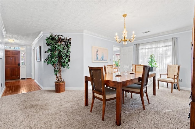 carpeted dining area with a textured ceiling, ornamental molding, and an inviting chandelier