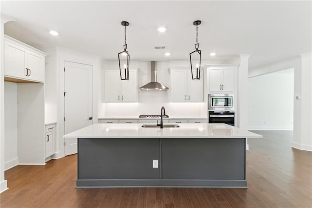 kitchen with wall chimney range hood, white cabinets, and a kitchen island with sink