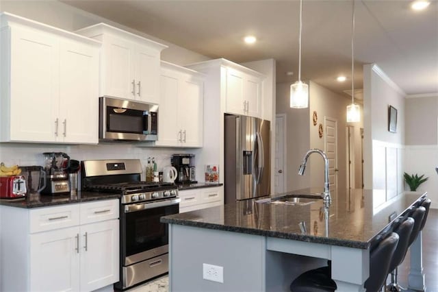 kitchen featuring appliances with stainless steel finishes, dark stone counters, sink, decorative light fixtures, and white cabinets