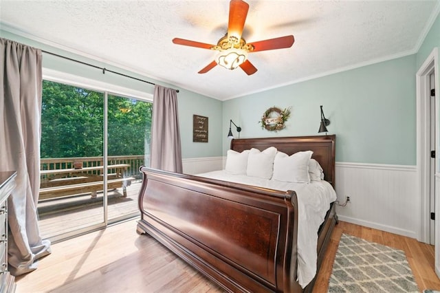 bedroom with access to exterior, a textured ceiling, wood finished floors, a wainscoted wall, and ceiling fan