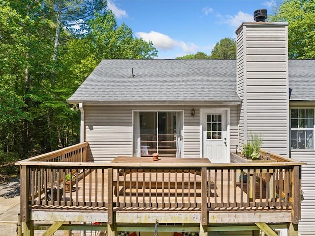 rear view of house with roof with shingles, a wooden deck, and a chimney