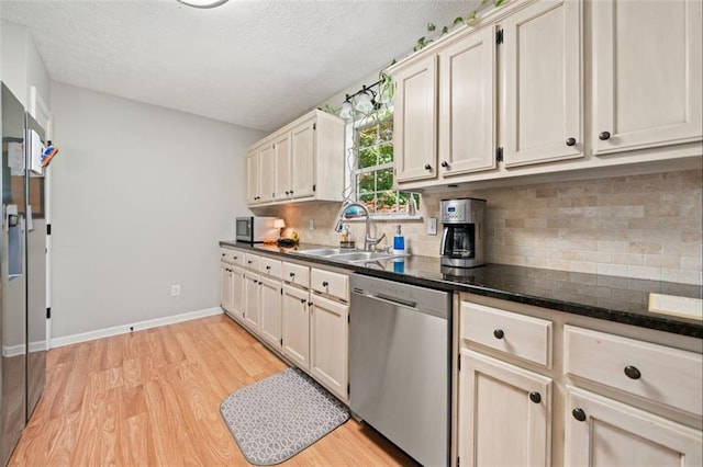 kitchen with stainless steel appliances, a sink, light wood finished floors, decorative backsplash, and a textured ceiling