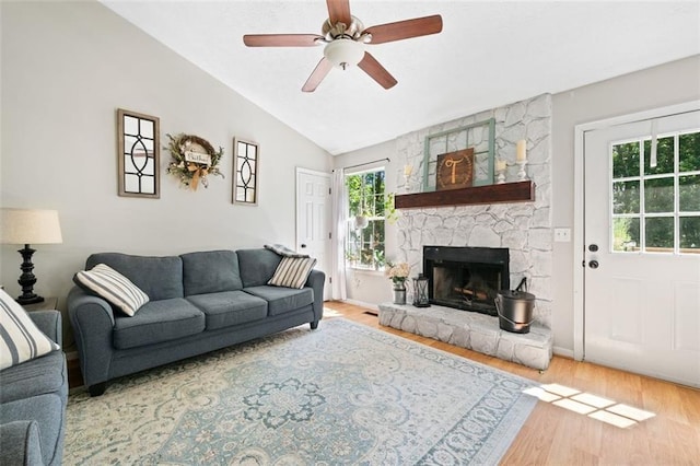 living area with wood finished floors, vaulted ceiling, a stone fireplace, and a ceiling fan