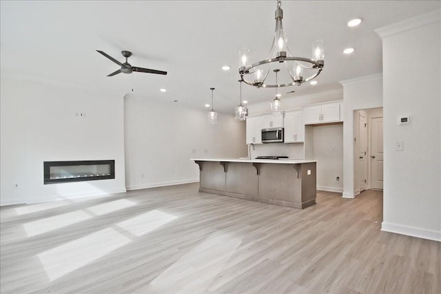 kitchen featuring a center island with sink, a breakfast bar, a glass covered fireplace, stainless steel microwave, and open floor plan