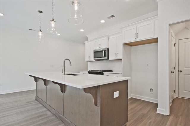 kitchen featuring a sink, stainless steel microwave, light wood-style floors, and a center island with sink