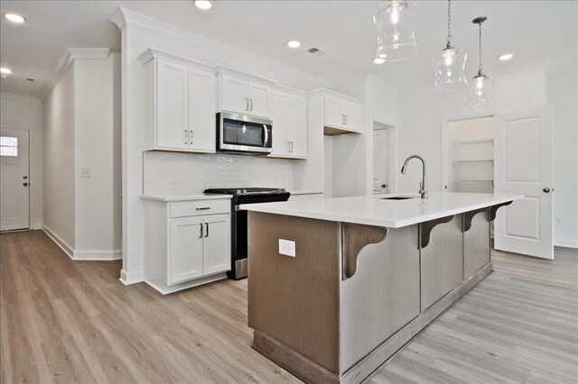 kitchen with an island with sink, a sink, stainless steel appliances, white cabinets, and crown molding