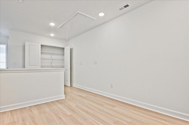 empty room with light wood finished floors, visible vents, attic access, and baseboards