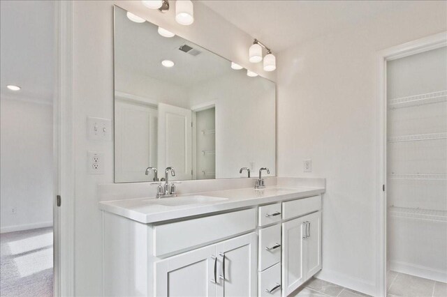 full bath with double vanity, visible vents, a walk in closet, and a sink