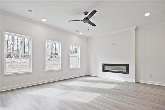 unfurnished living room featuring a glass covered fireplace, wood finished floors, baseboards, and ornamental molding