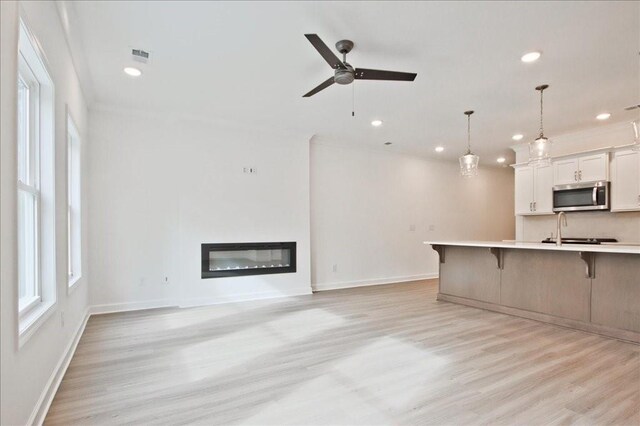 unfurnished living room featuring light wood-type flooring, visible vents, a glass covered fireplace, recessed lighting, and baseboards