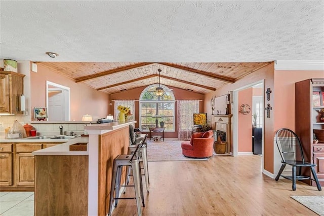 kitchen with a kitchen bar, a textured ceiling, vaulted ceiling with beams, and light hardwood / wood-style flooring