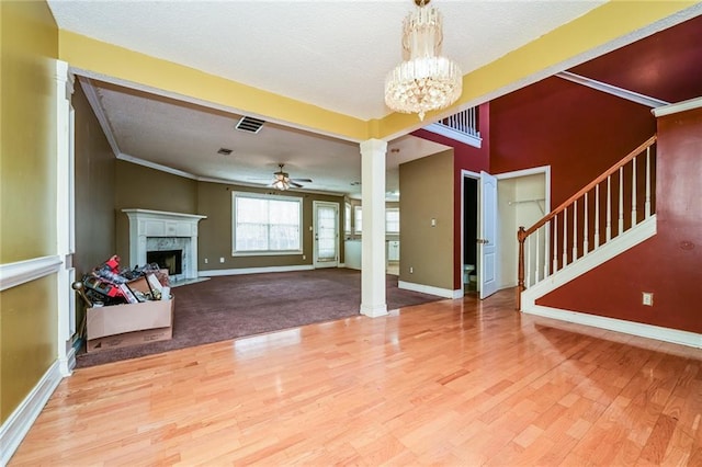 unfurnished living room featuring crown molding, hardwood / wood-style flooring, a fireplace, ceiling fan with notable chandelier, and ornate columns