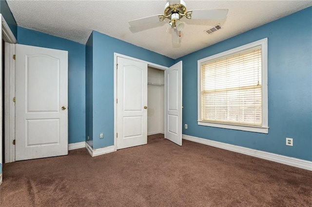 unfurnished bedroom with dark colored carpet, ceiling fan, a textured ceiling, and a closet