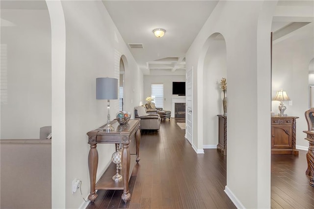 corridor with beamed ceiling, coffered ceiling, and dark wood-type flooring