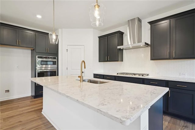 kitchen featuring wall chimney exhaust hood, hanging light fixtures, and an island with sink