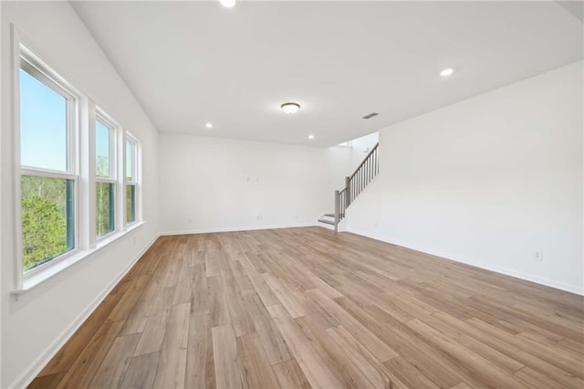 empty room with recessed lighting, light wood-style flooring, baseboards, and stairs