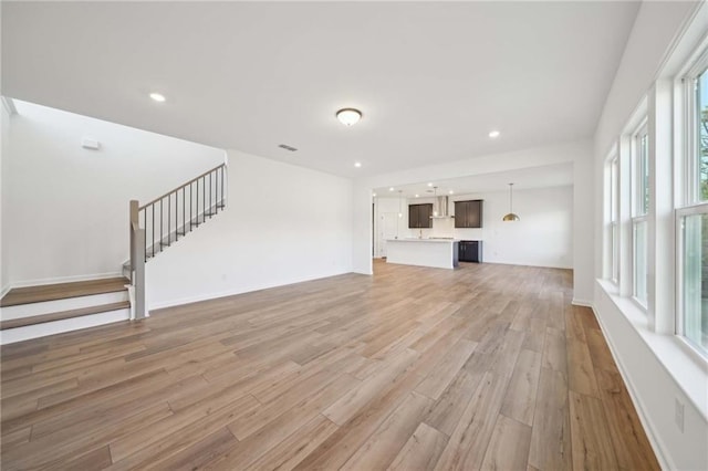 unfurnished living room with baseboards, stairway, recessed lighting, and light wood-style floors