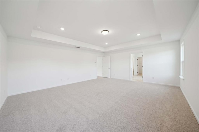 empty room with recessed lighting, a tray ceiling, baseboards, and light colored carpet