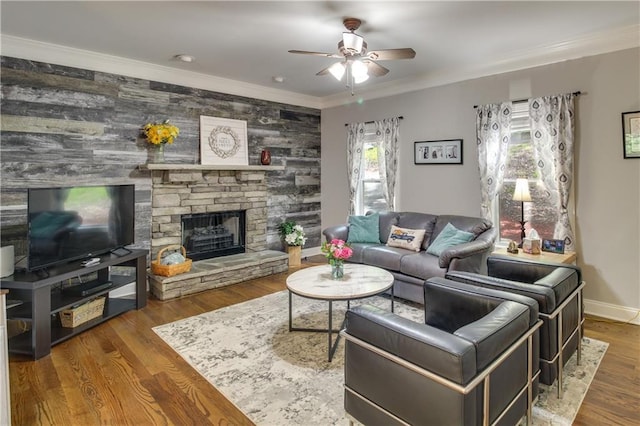 living room featuring ceiling fan, wood-type flooring, a stone fireplace, and ornamental molding