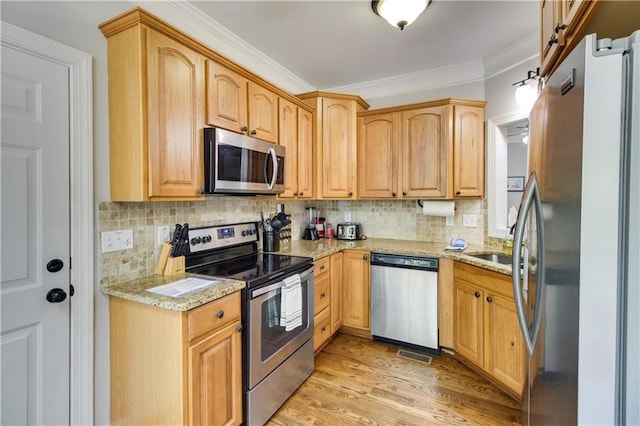 kitchen with light stone countertops, stainless steel appliances, tasteful backsplash, ornamental molding, and light hardwood / wood-style flooring