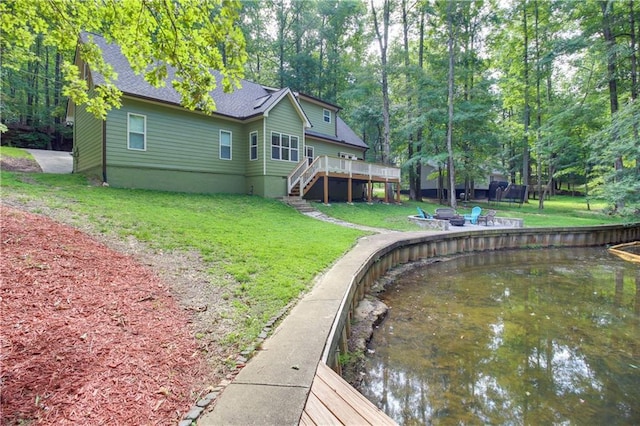 rear view of house with an outdoor fire pit, a deck with water view, and a yard