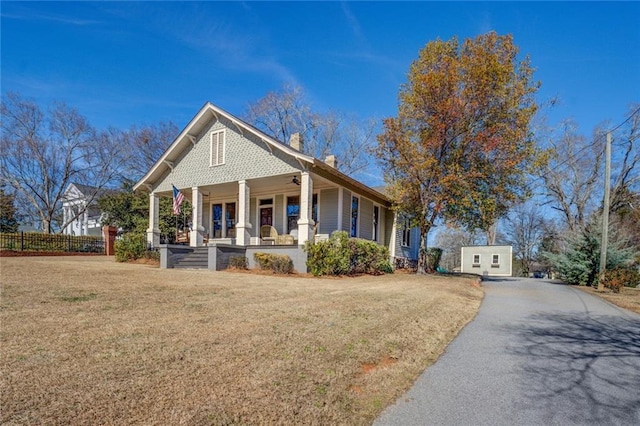 view of front of home featuring a porch, a storage unit, and a front lawn