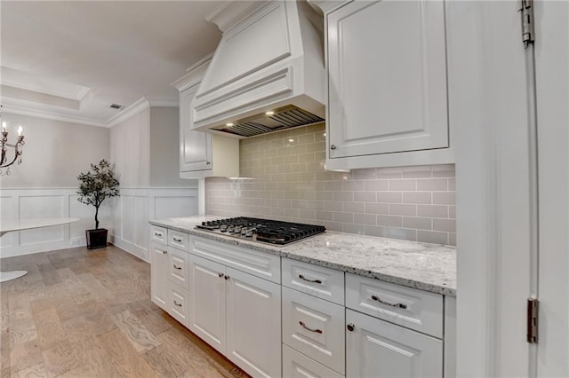 kitchen with crown molding, stainless steel gas cooktop, white cabinetry, backsplash, and custom exhaust hood