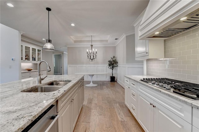 kitchen with a sink, light wood finished floors, premium range hood, stainless steel appliances, and ornamental molding