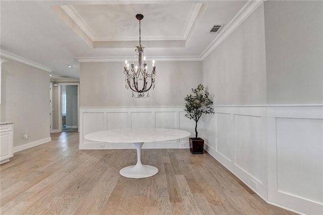 unfurnished dining area featuring light wood-style floors, visible vents, crown molding, an inviting chandelier, and a decorative wall