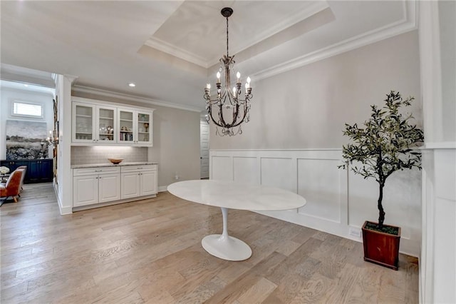 dining space featuring crown molding, a raised ceiling, light wood-style floors, and an inviting chandelier