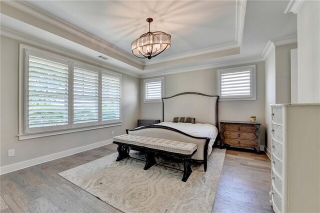bedroom with visible vents, crown molding, wood finished floors, a chandelier, and a tray ceiling