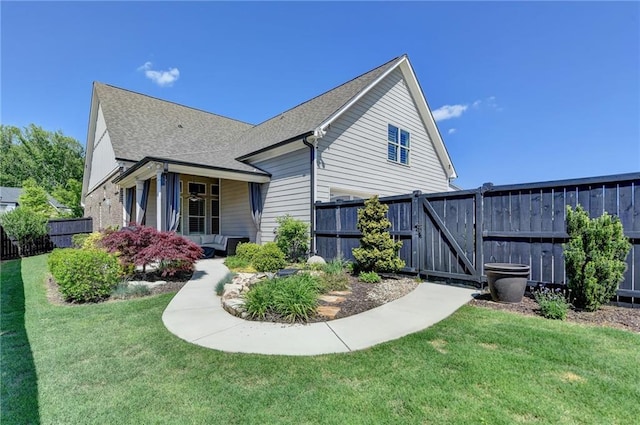 view of side of home featuring fence, a gate, a yard, and roof with shingles