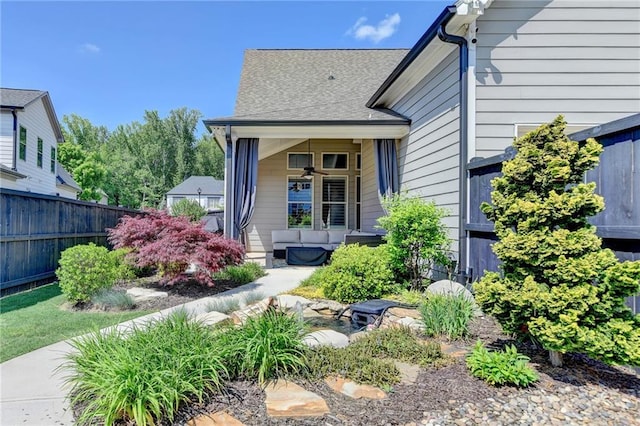 doorway to property with fence, a ceiling fan, and a shingled roof