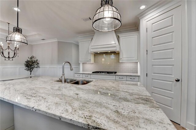 kitchen with light stone countertops, a sink, white cabinetry, visible vents, and ornamental molding