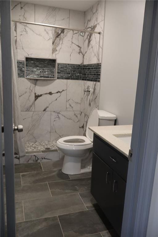 bathroom with tiled shower, vanity, and toilet