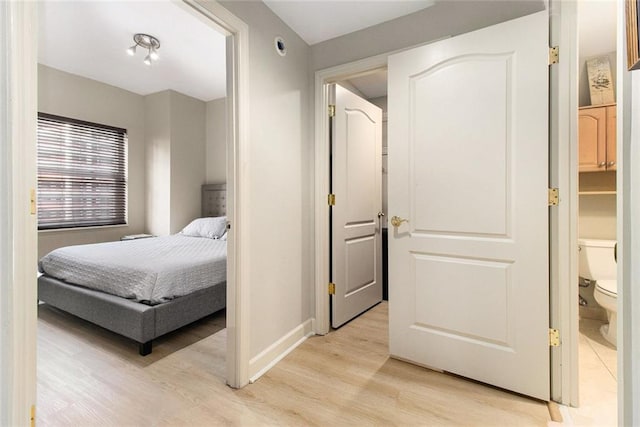 bedroom featuring baseboards, ensuite bath, and light wood-style floors