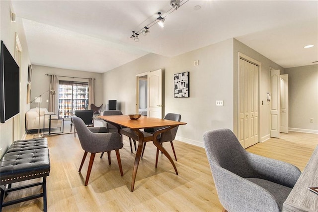 dining space with baseboards, light wood-type flooring, and rail lighting