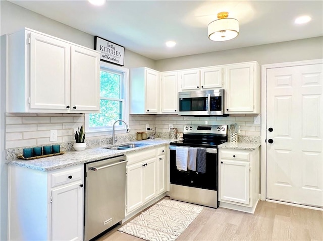 kitchen featuring decorative backsplash, stainless steel appliances, sink, light wood-type flooring, and white cabinets