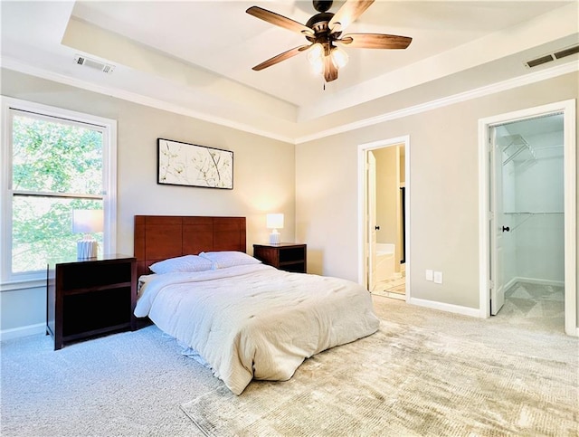 carpeted bedroom with a closet, a walk in closet, a tray ceiling, ensuite bath, and ceiling fan