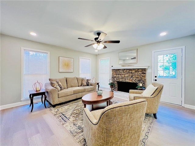 living room with light hardwood / wood-style floors, a stone fireplace, and ceiling fan